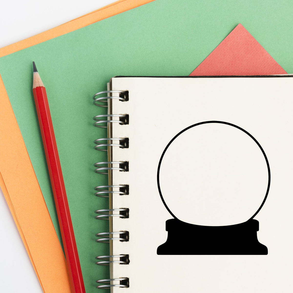 Red pencil beside green and orange notebooks with spiral pad and black stamp and seal icon