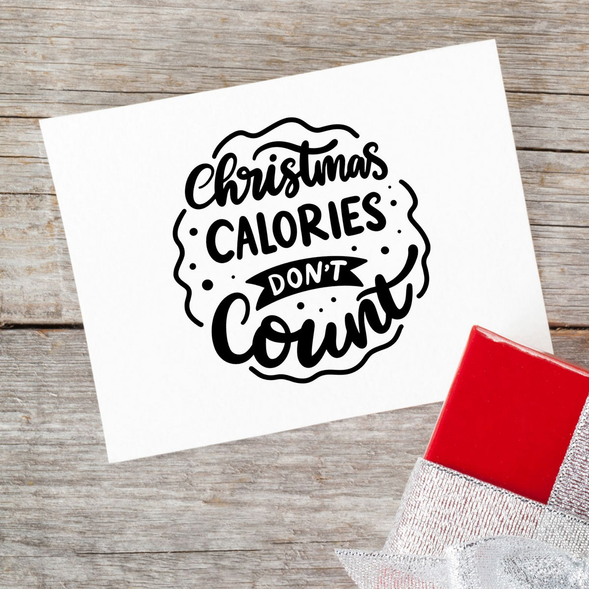 Black Christmas Calories Dont Count stamp design on white paper, with a red seal block on rustic wood.