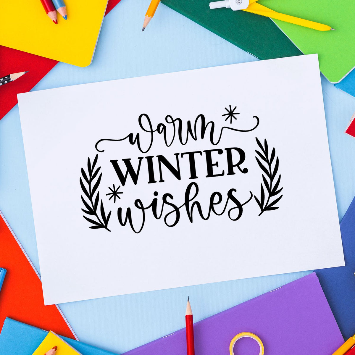Warm winter wishes stamp and seal on white card, framed by colorful pencils and paper in red, yellow, green, blue, and purple.