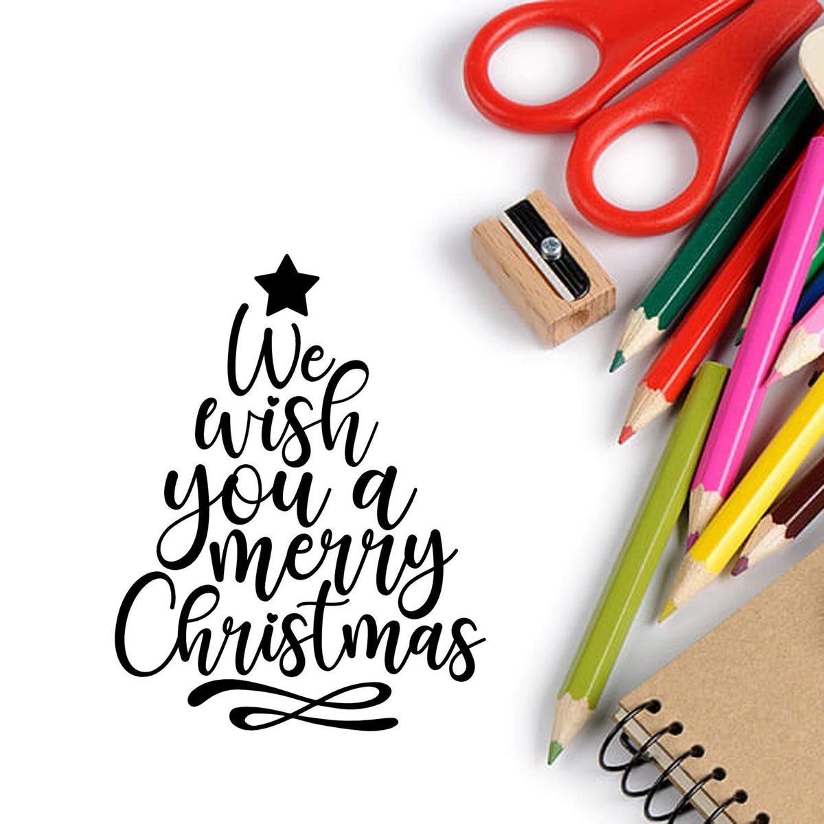 Black We wish you a merry Christmas stamp/seal with red scissors, colorful pencils, and notebook on white background.