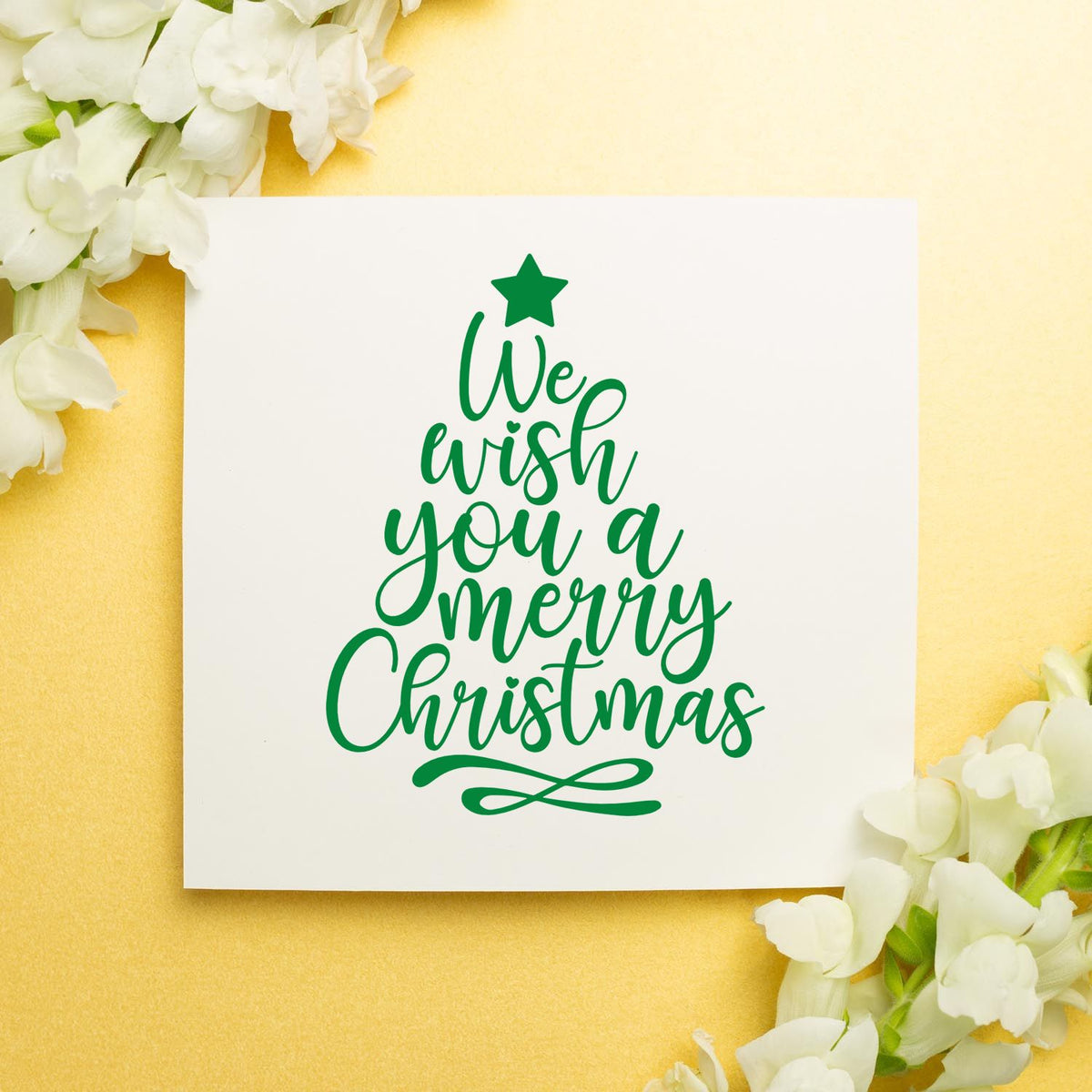 Green Christmas stamp and seal design on white card, tree-shaped text with star, on pale yellow background with white flowers.