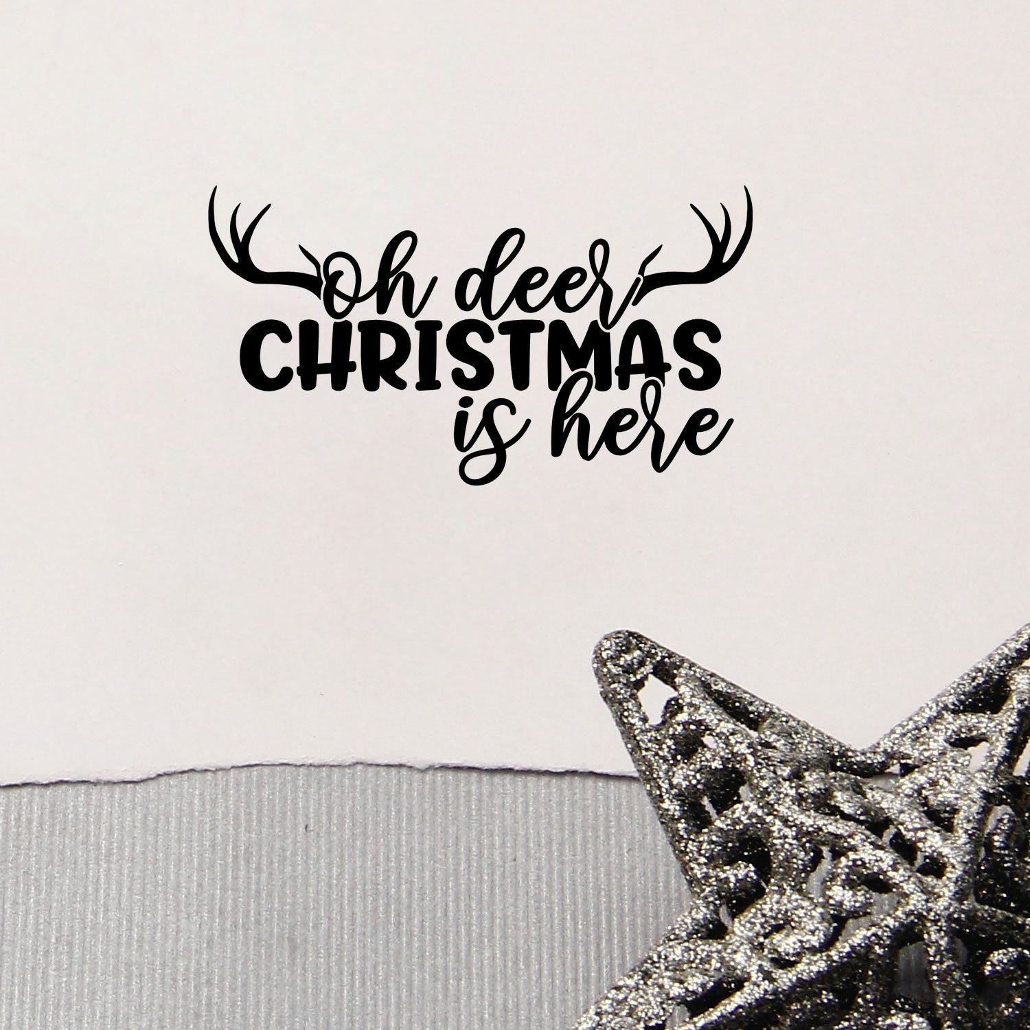 Black Oh deer Christmas is here stamp with antlers and glittery silver star seal on white background