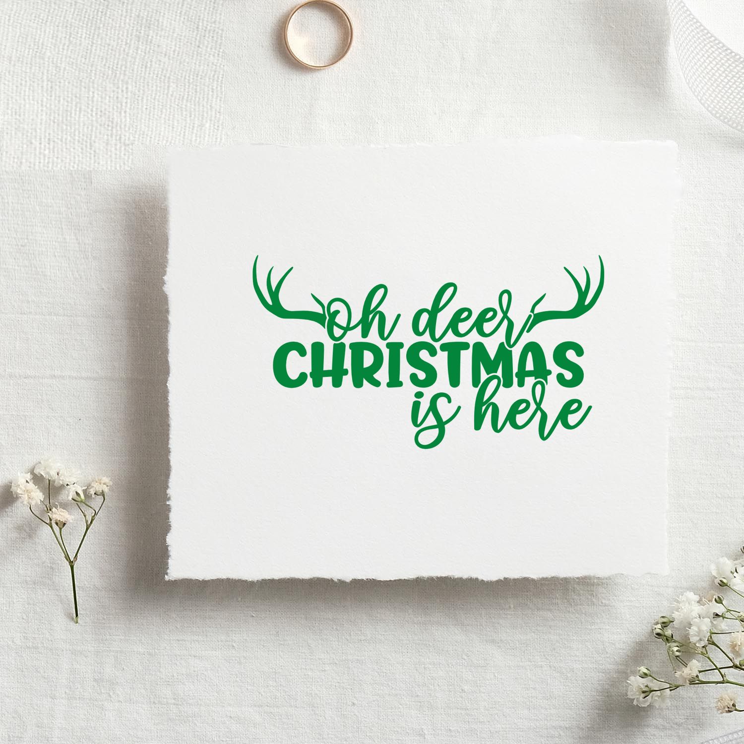 Green deer antler Christmas stamp and seal design on white textured paper with Oh deer Christmas is here text.