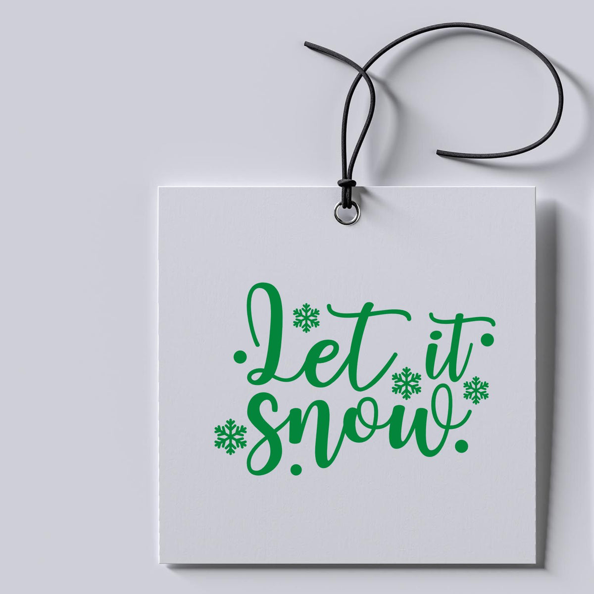 White hanging tag with black cord, featuring a green Let it snow stamp seal and snowflakes.