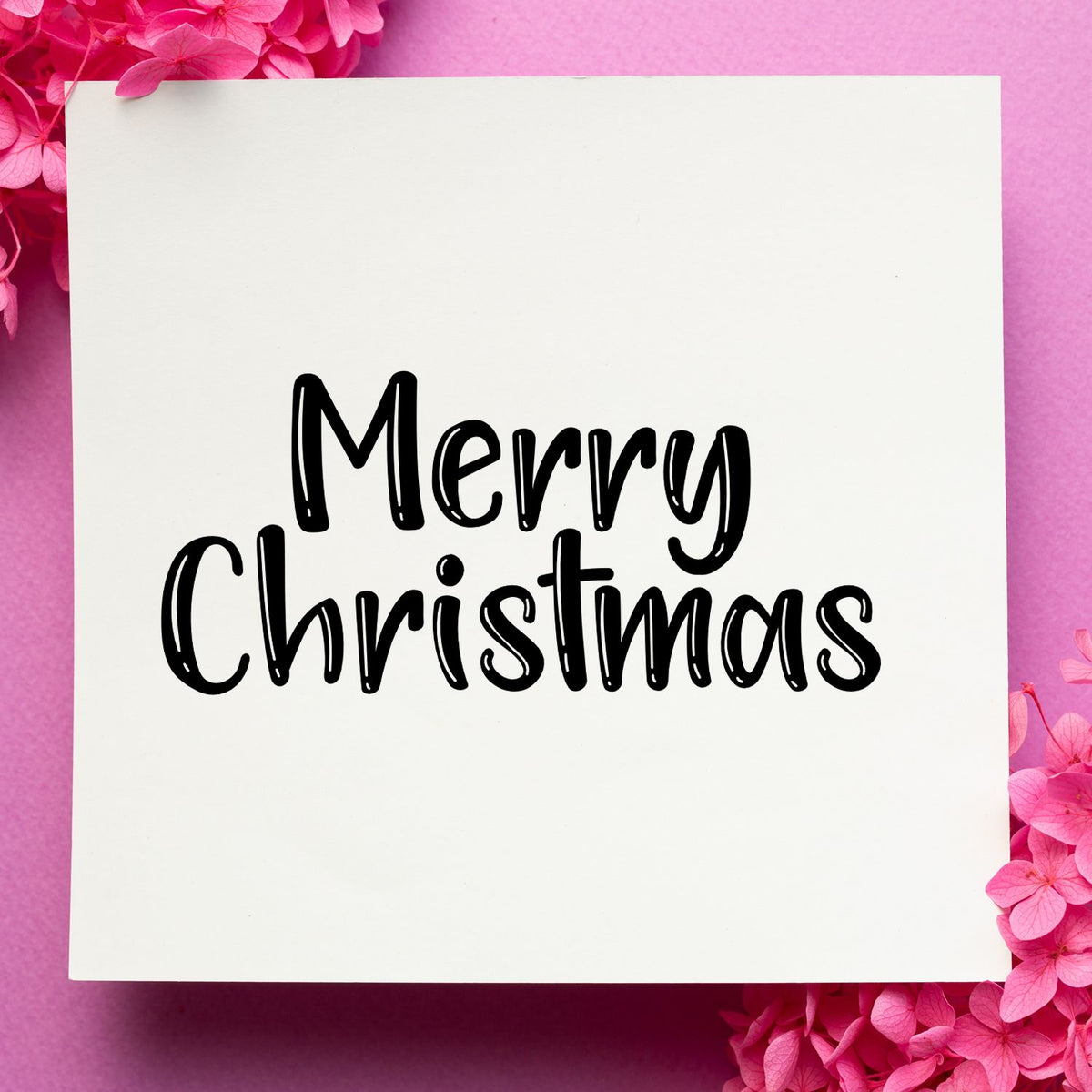 Black Merry Christmas stamp and seal on white card, framed by bright pink flowers on a pink background.