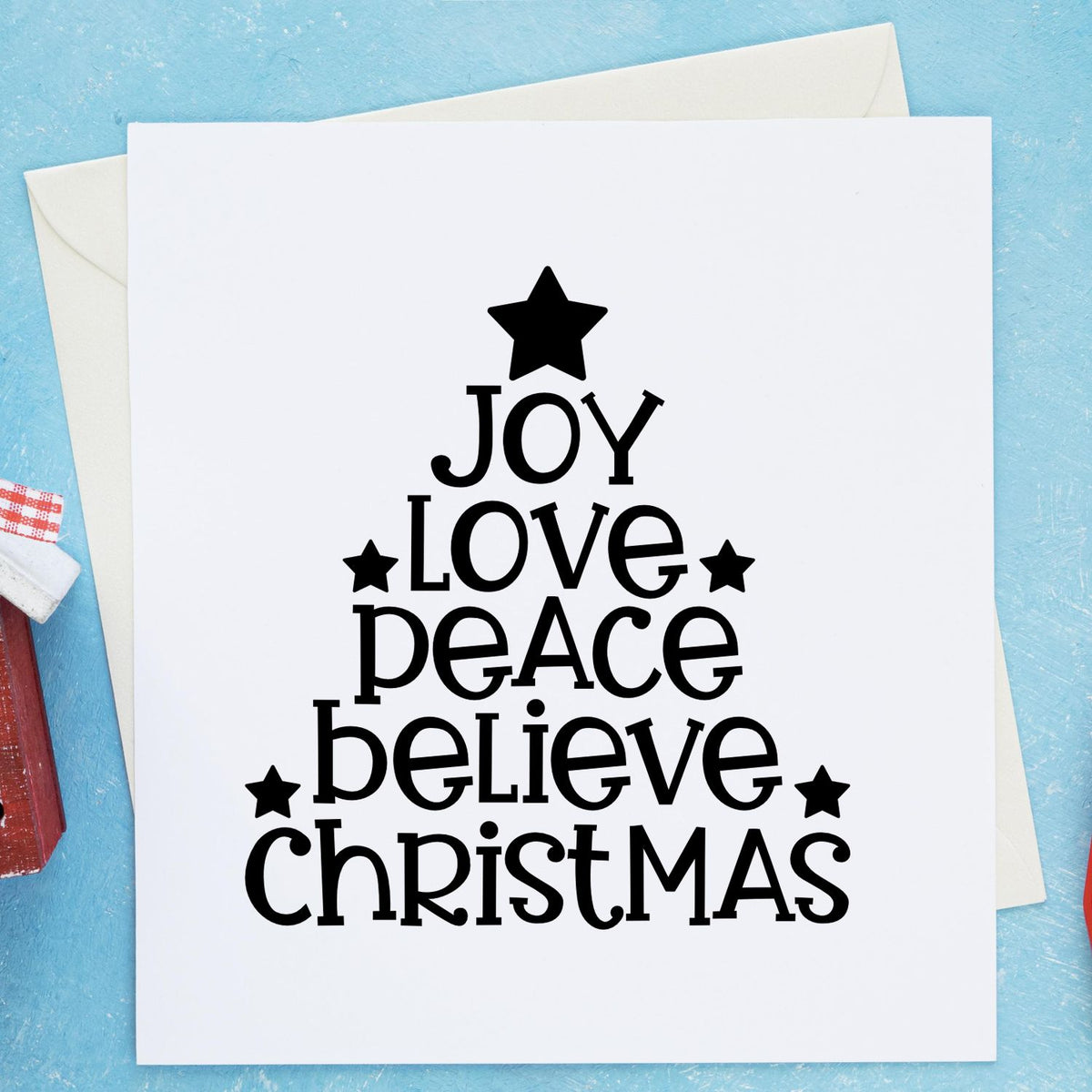 Black Christmas tree word art stamp and seal with Joy, Love, Peace, Believe, Christmas on white card, blue background, star accents