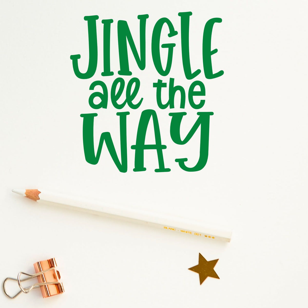 Green JINGLE all the WAY lettering with white pencil, copper binder clip and gold star seal on white background