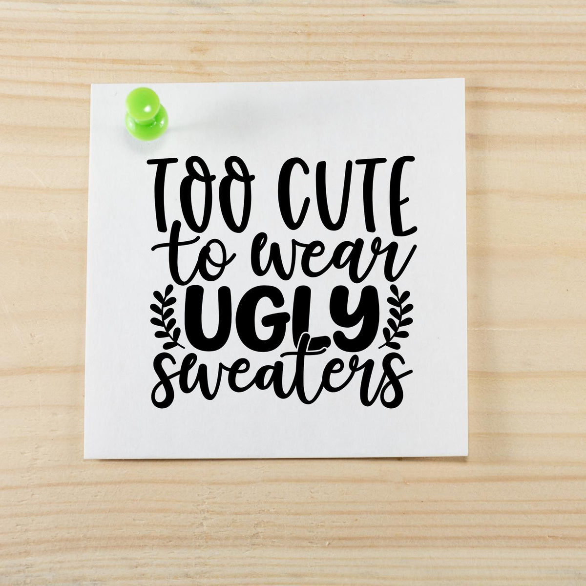 Black cute stamp/seal design reading Too Cute to Wear Ugly Sweaters on white paper with a green pushpin.