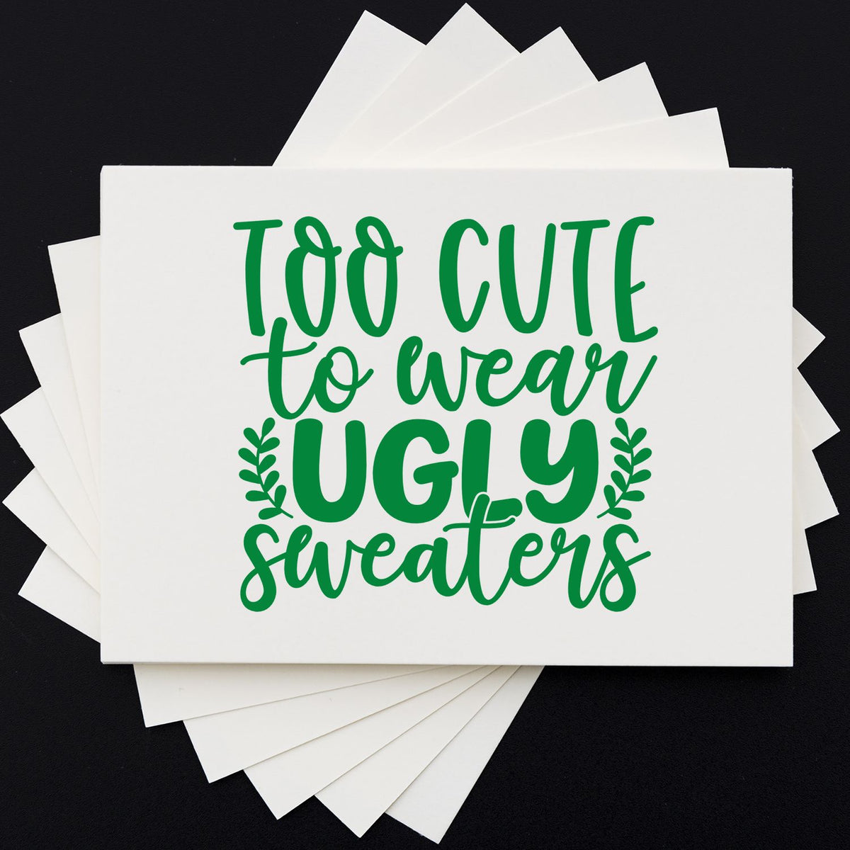 Green Too Cute to Wear Ugly Sweaters stamp and seal design on stacked white cards, black background.