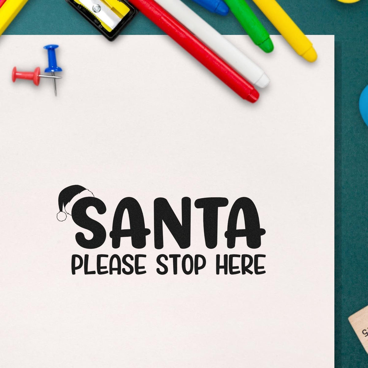 Black Santa stamp seal with Santa hat and PLEASE STOP HERE text, surrounded by colorful red, blue, green and yellow pens.