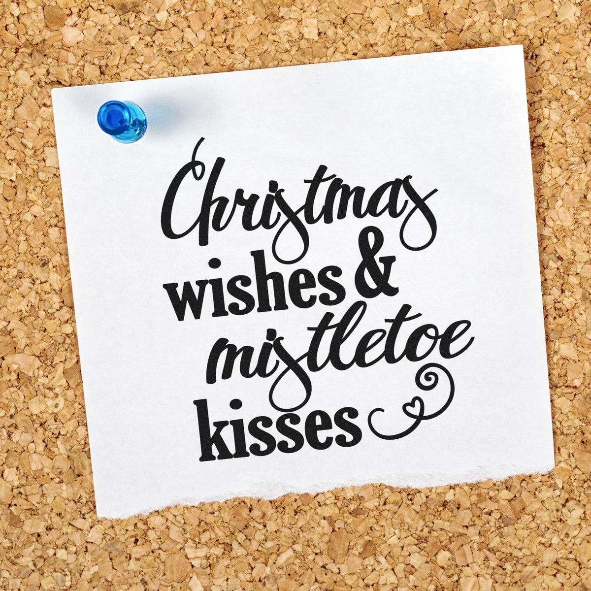 White paper stamp sample pinned to corkboard with blue push pin, showing black Christmas wishes & mistletoe kisses lettering.