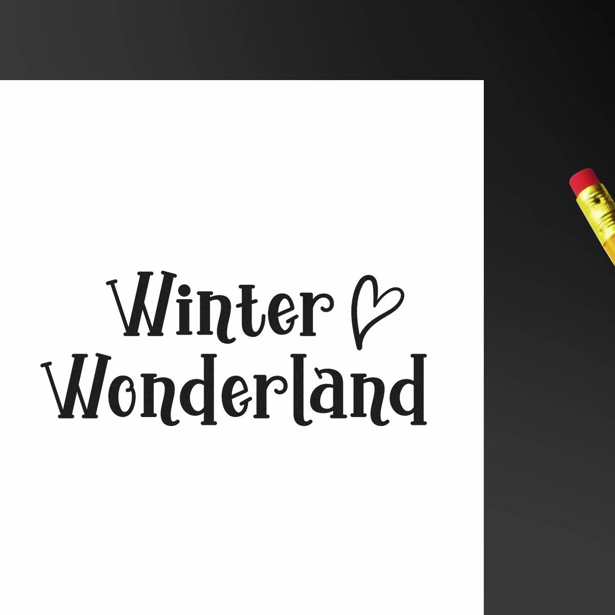 Black Winter Wonderland stamp with heart on white paper, beside a yellow pencil on dark background.