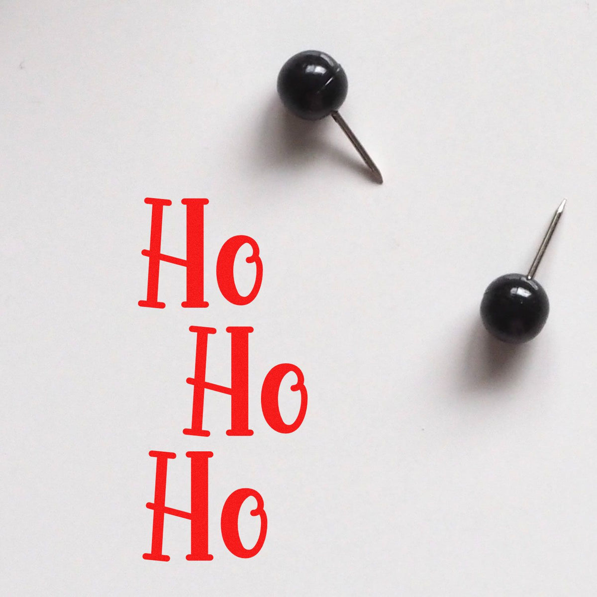 Red Ho Ho Ho stamp design with two black pushpin-style seal tools on a white background.