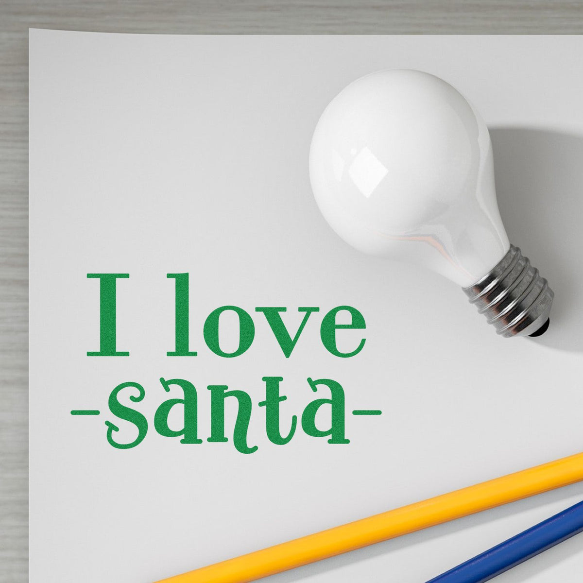 Green I love santa stamp and seal with white light bulb, on white paper, accented by yellow and blue pencils.