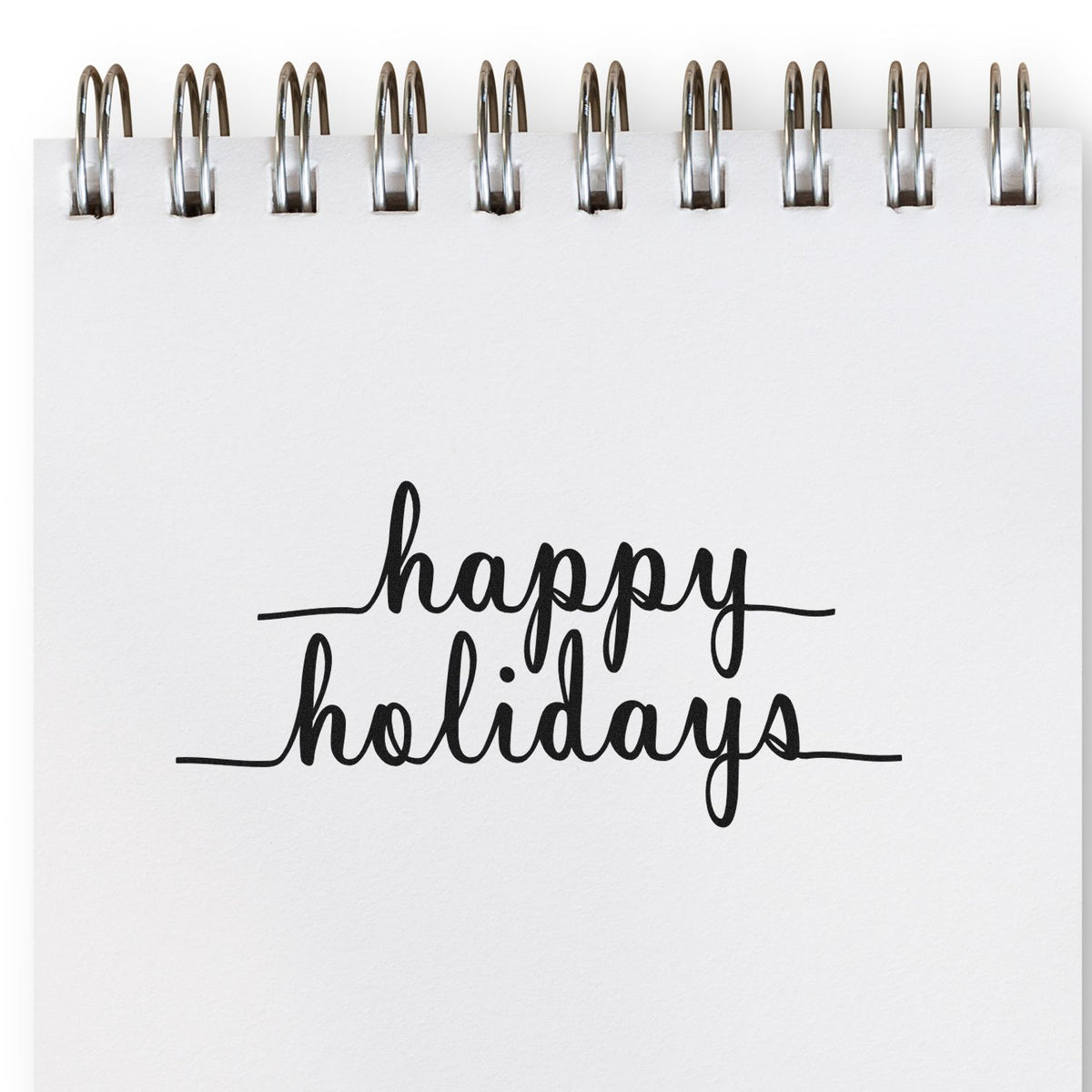 White spiral-bound notebook page with black happy holidays script stamp/seal design