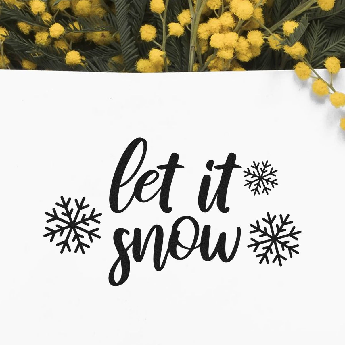 Black let it snow holiday stamp and seal design with snowflakes on a white background, framed by yellow mimosa flowers.