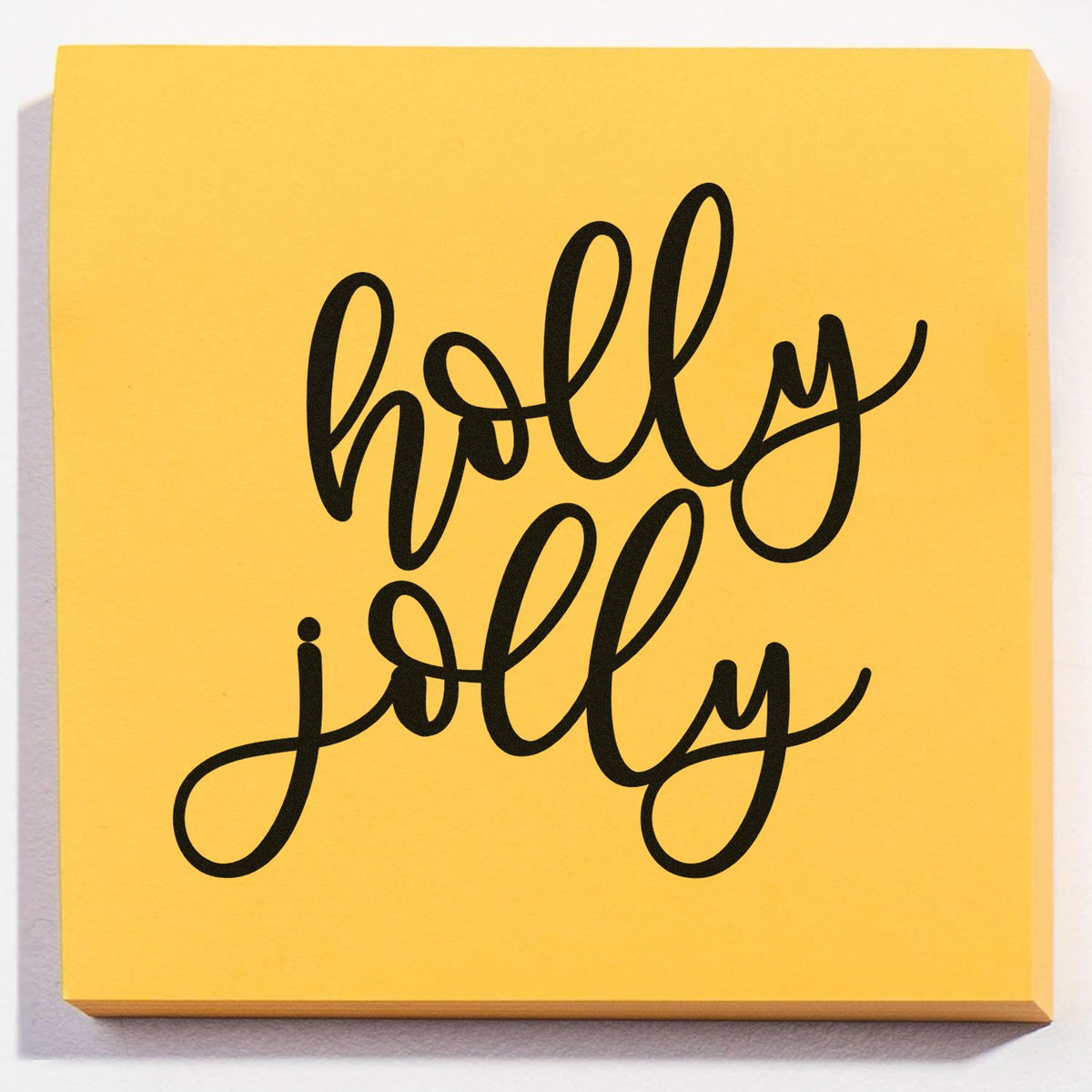 Yellow square stamp and seal pad with black cursive holly jolly lettering, bold festive design.