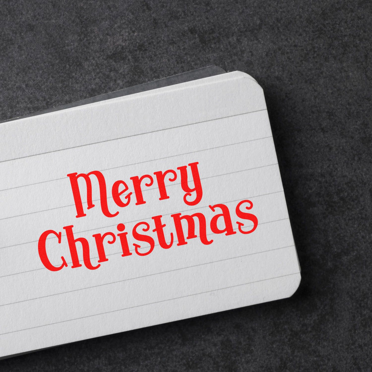 Red Merry Christmas stamp and seal on white lined card with rounded corners, on a dark textured background.