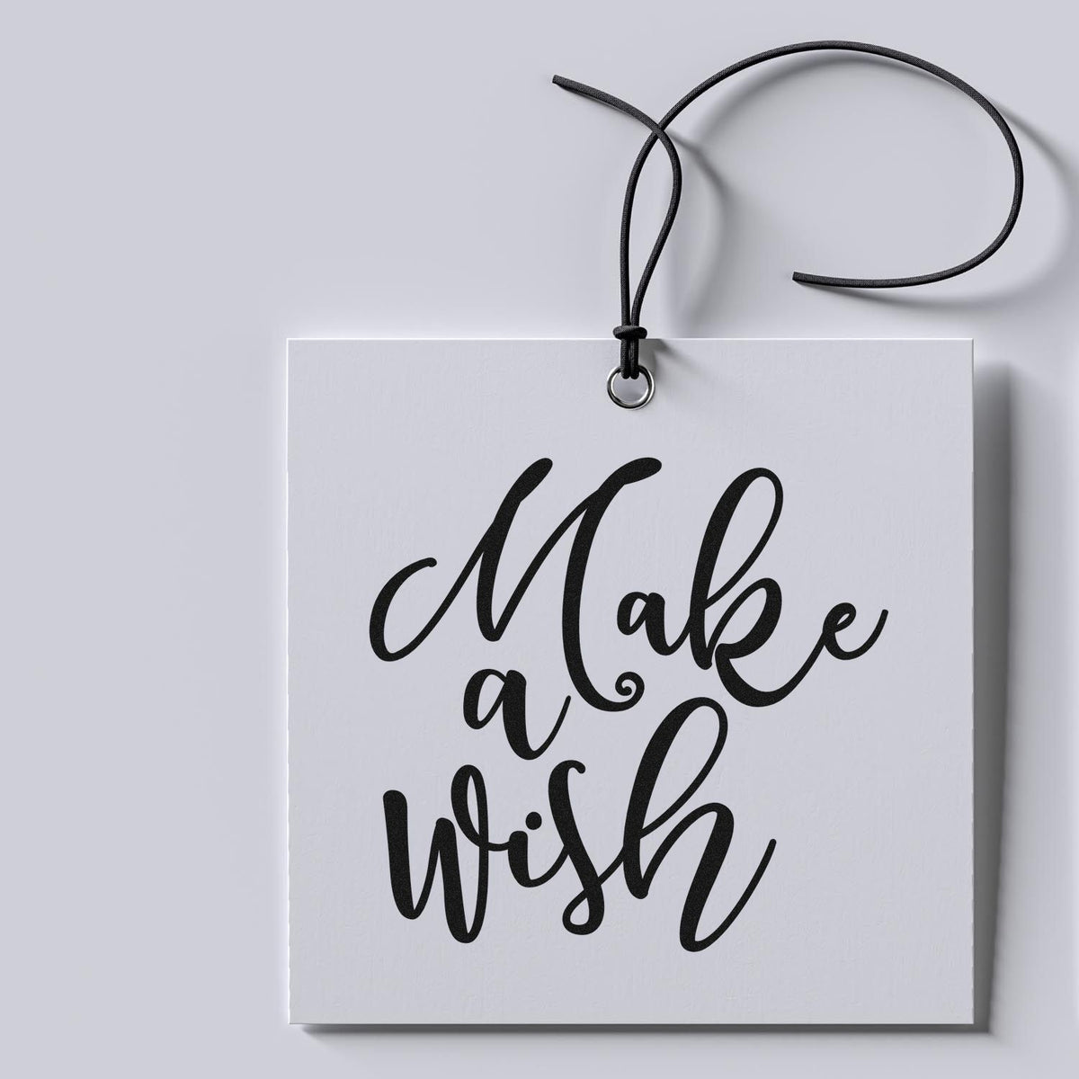 White stamp-and-seal tag with black cord and black script reading Make a Wish on a light gray background.
