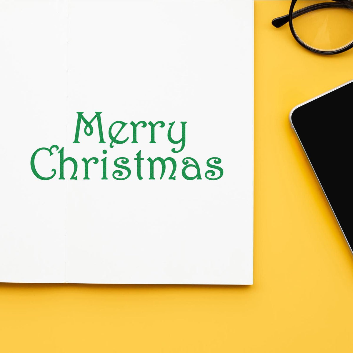 Green Merry Christmas stamp and seal on white paper, with black glasses and smartphone on a bright yellow background.