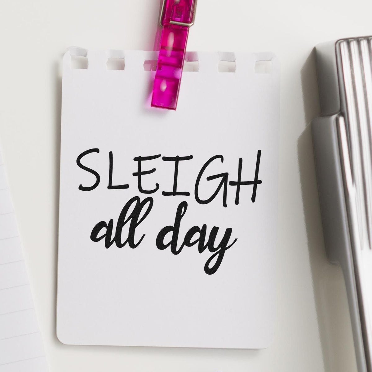 White stamp and seal card clipped with a pink clip, featuring black SLEIGH all day lettering and a silver stamp tool.