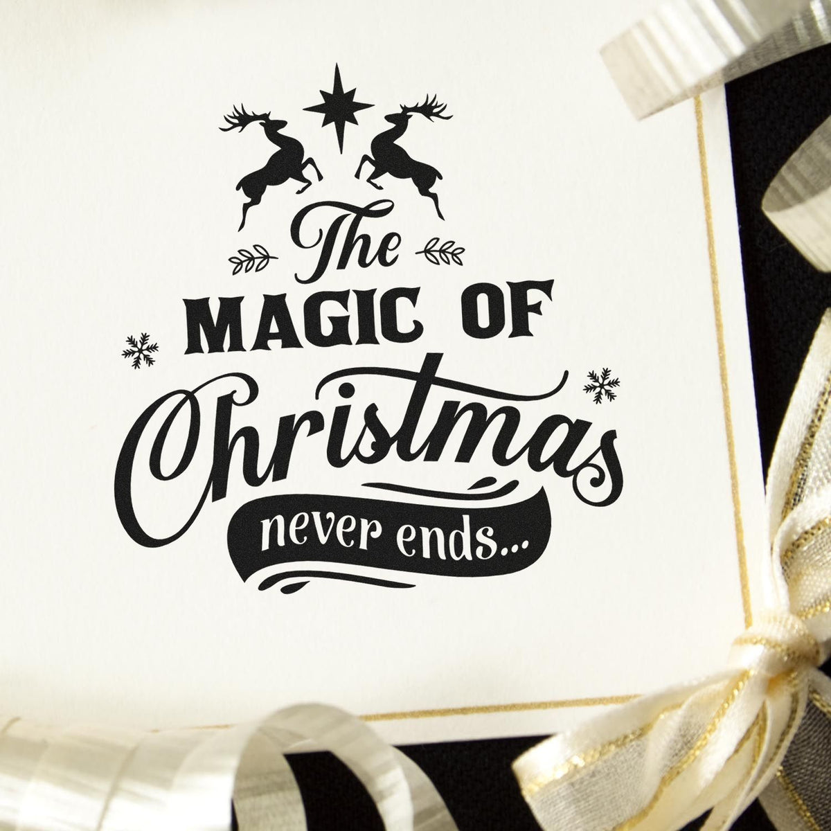 Black Christmas stamp seal on white card with deer, star, and The Magic of Christmas never ends text, accented by gold ribbon.