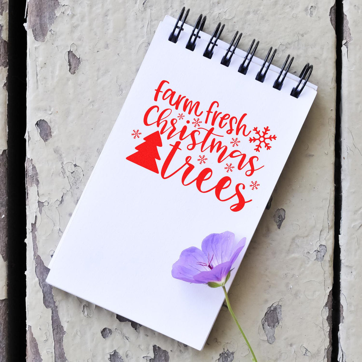 Red farm fresh Christmas trees stamp design on white spiral notebook, black rings, with purple flower accent.