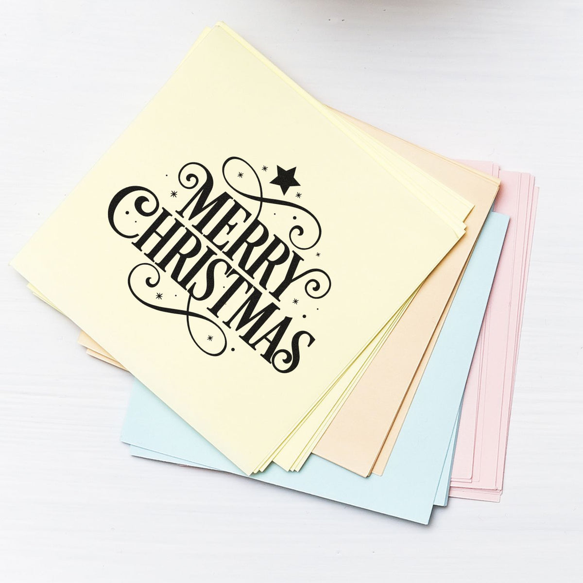 Stack of pastel yellow, blue, pink and beige stamp cards with black Merry Christmas seal design