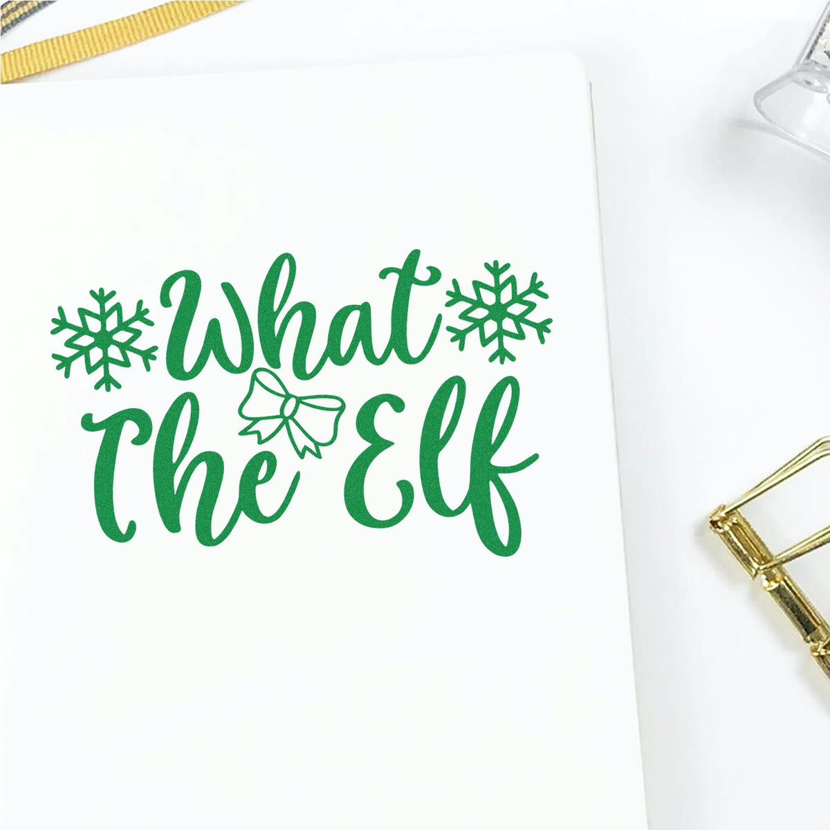 Green holiday stamp and seal design reading What the Elf with snowflakes and bow on a white background