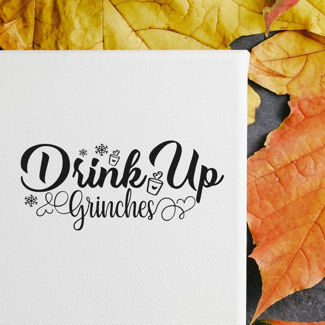 Black holiday stamp and seal reading Drink Up Grinches on white textured paper with yellow and orange leaves.