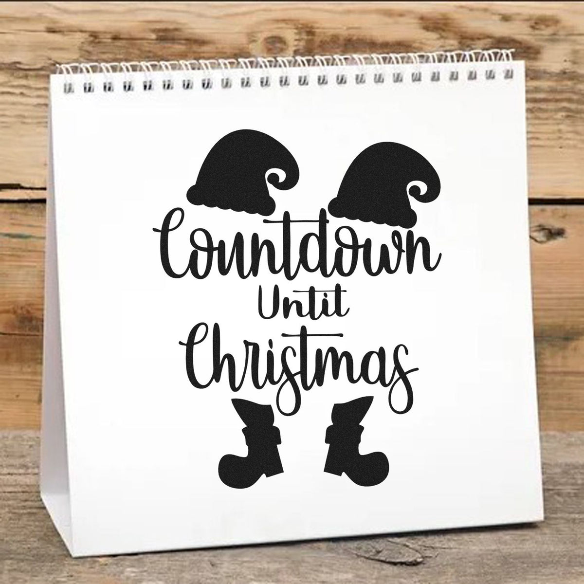 White spiral gift bag with black custom stamp and seal reading Countdown Until Christmas, with Santa hats and boots.