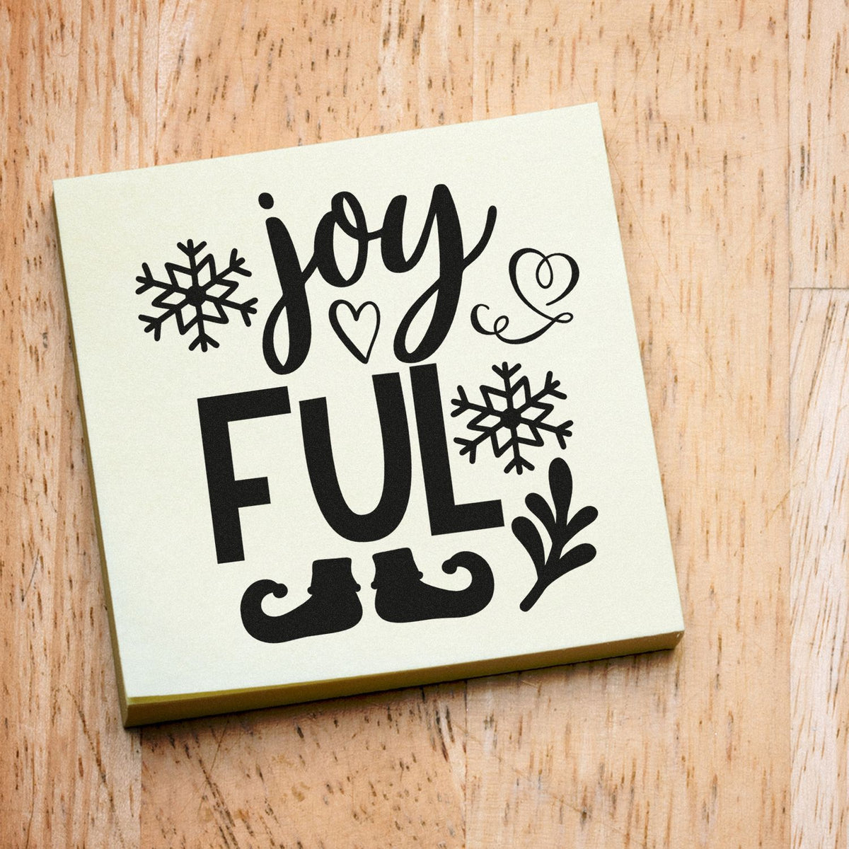 Holiday stamp and seal with black Joyful design, snowflakes, heart, elf boots, and holly on a cream square.