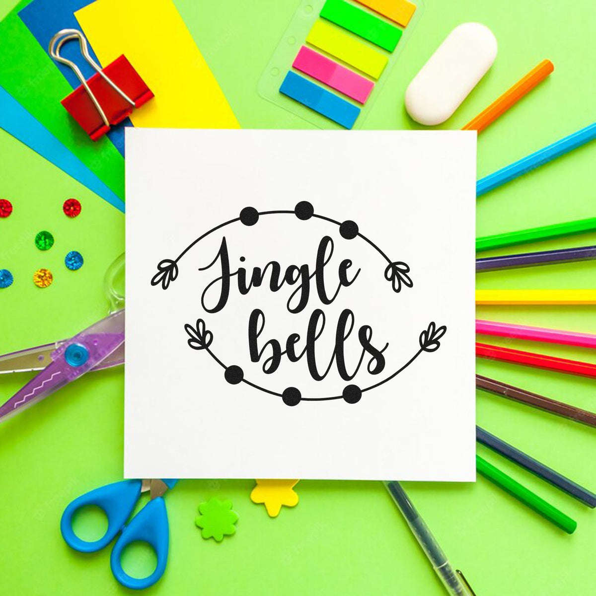 Jingle bells stamp and seal design on white paper, surrounded by colorful stationery on bright green background.