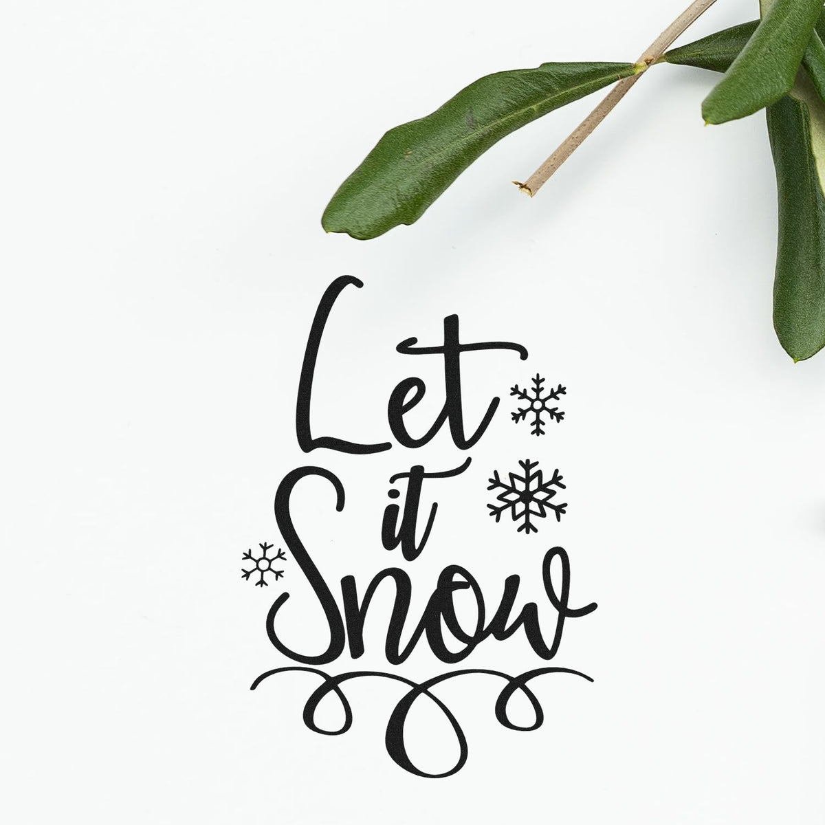 Black Let it Snow stamp seal with snowflakes on a white background, framed by green leaves