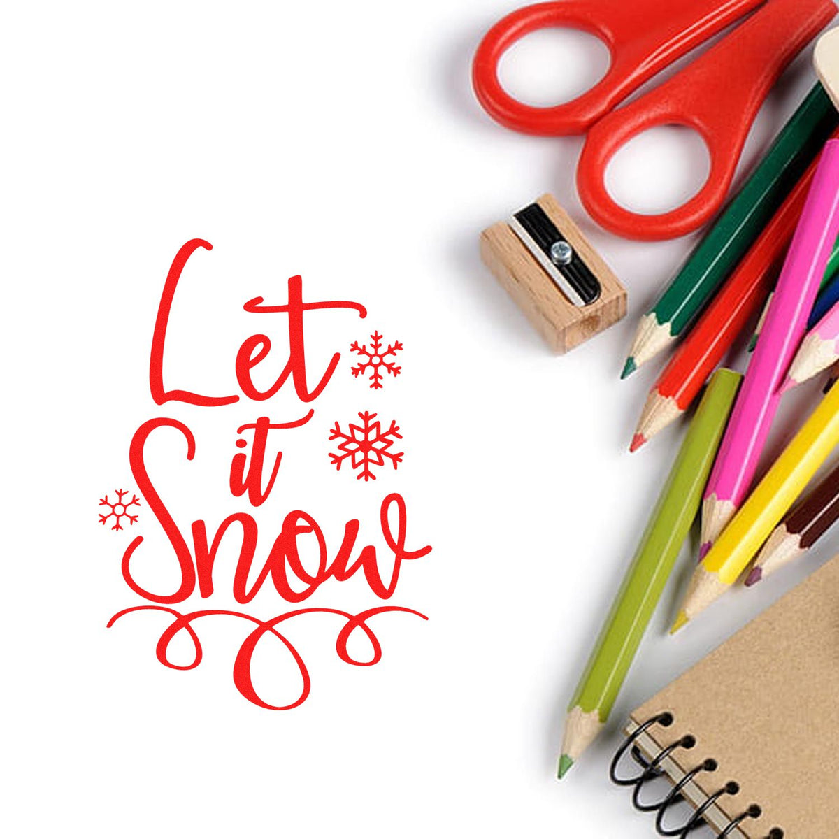 Red Let it Snow holiday stamp and seal with snowflakes, beside colorful pencils, scissors, sharpener and notebook.