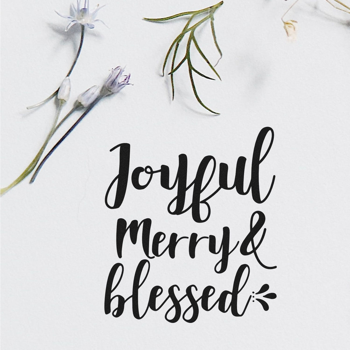 Black script stamp and seal reading Joyful Merry & blessed with delicate white and green floral accents on a white background.
