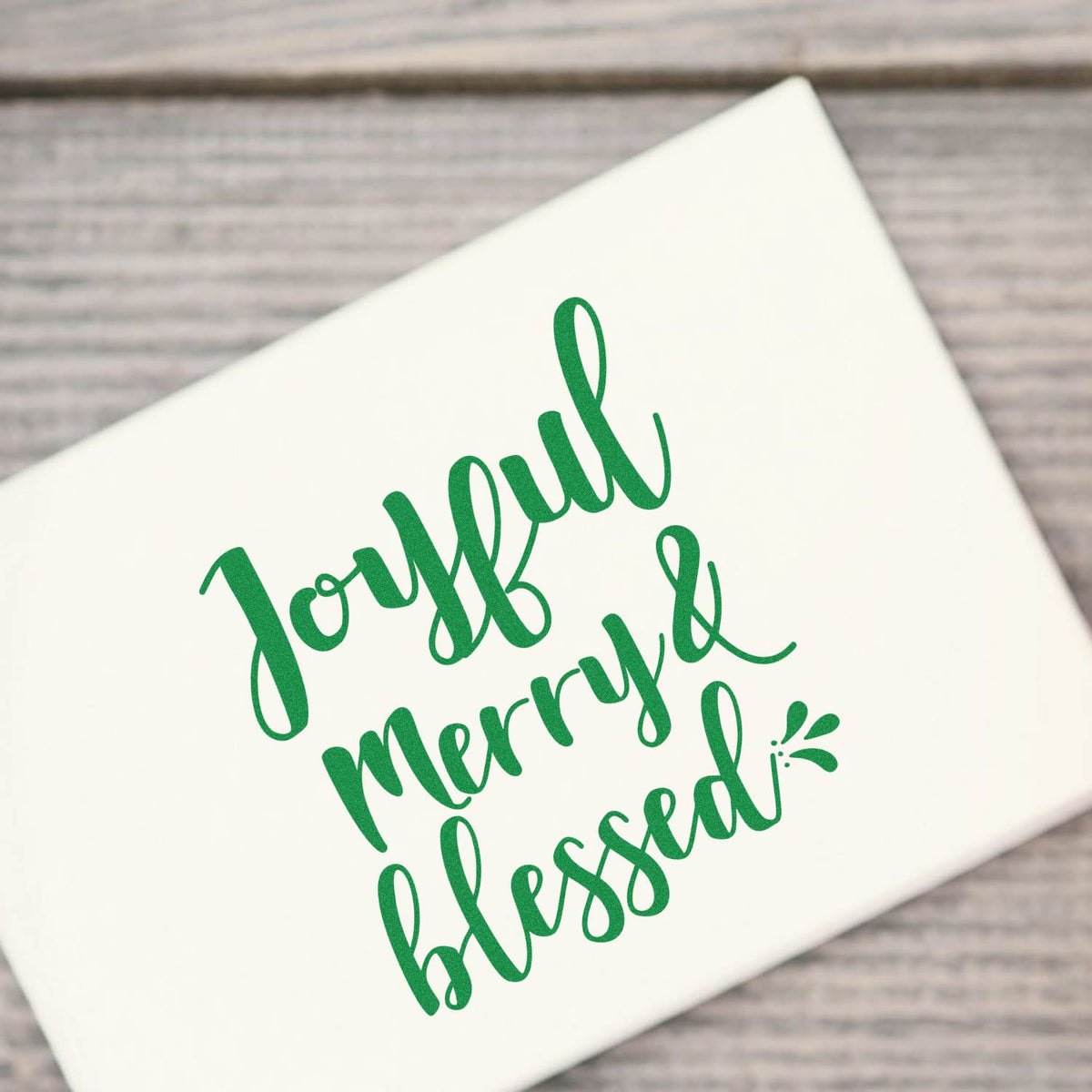 Cream stamp seal with green Joyful merry & blessed script on rustic wood background.