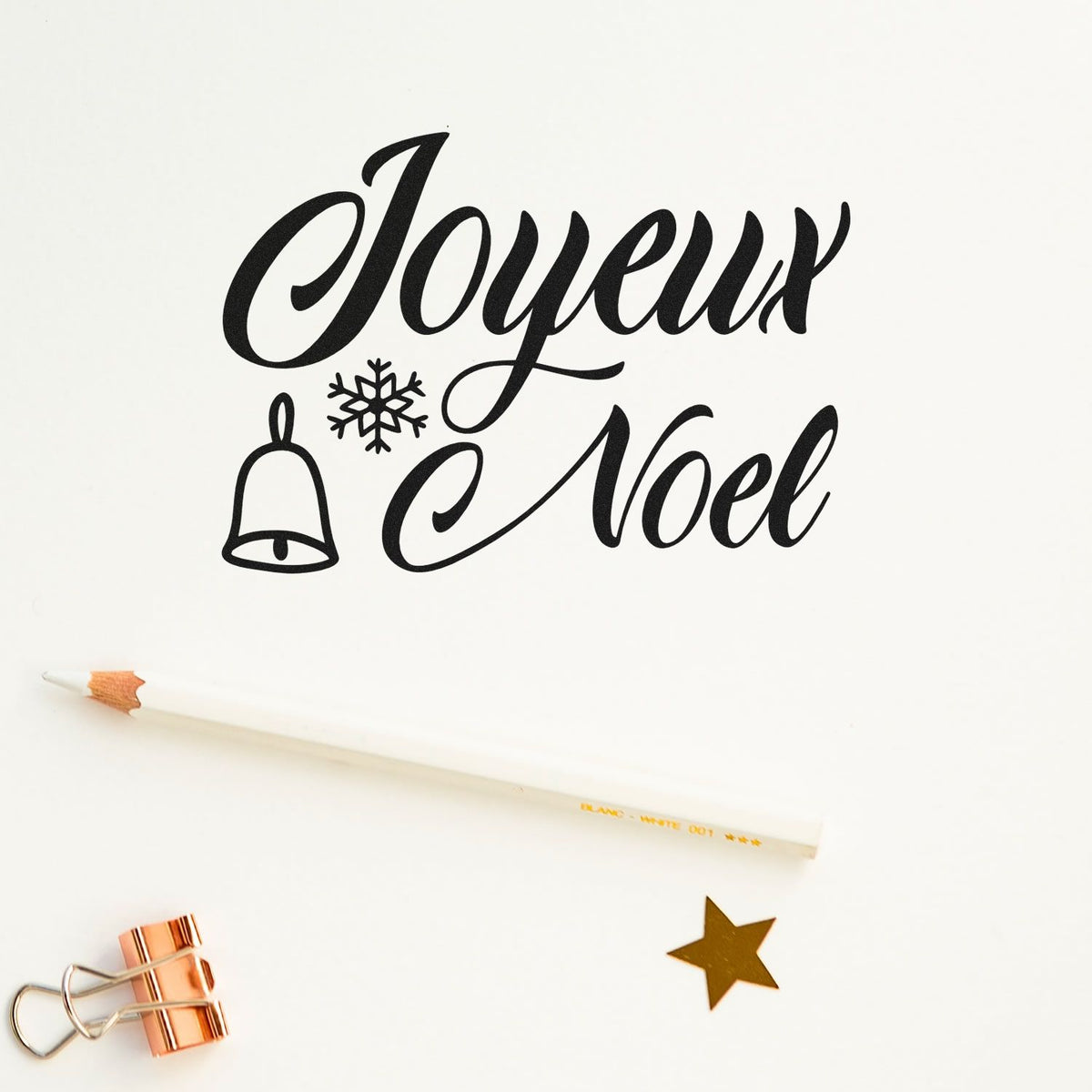 Black Joyeux Noel holiday stamp design with bell and snowflake, on white paper with gold star seal.