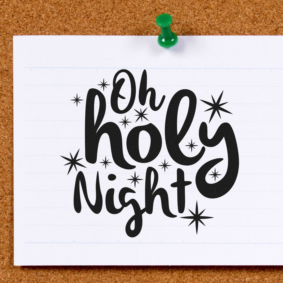 Decorative black Oh Holy Night stamp design with starbursts on white paper, pinned to corkboard with a green pushpin.