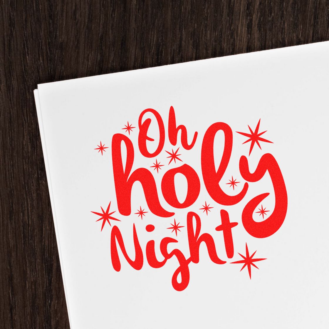 Red Oh Holy Night stamp and seal design with starbursts on white paper against a dark wood background.