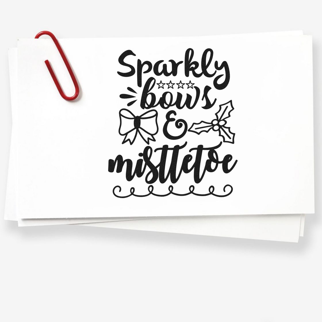 Black holiday stamp-and-seal design on white paper, with bows and mistletoe, clipped by a red paperclip.