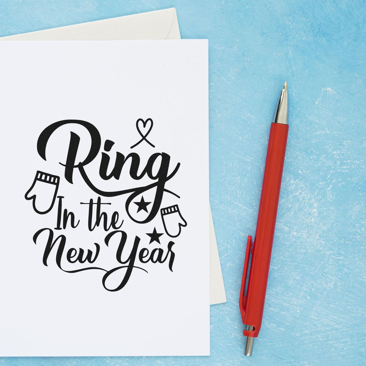 Black New Year stamp and seal design with mittens and stars on white card, beside a red pen on light blue background.
