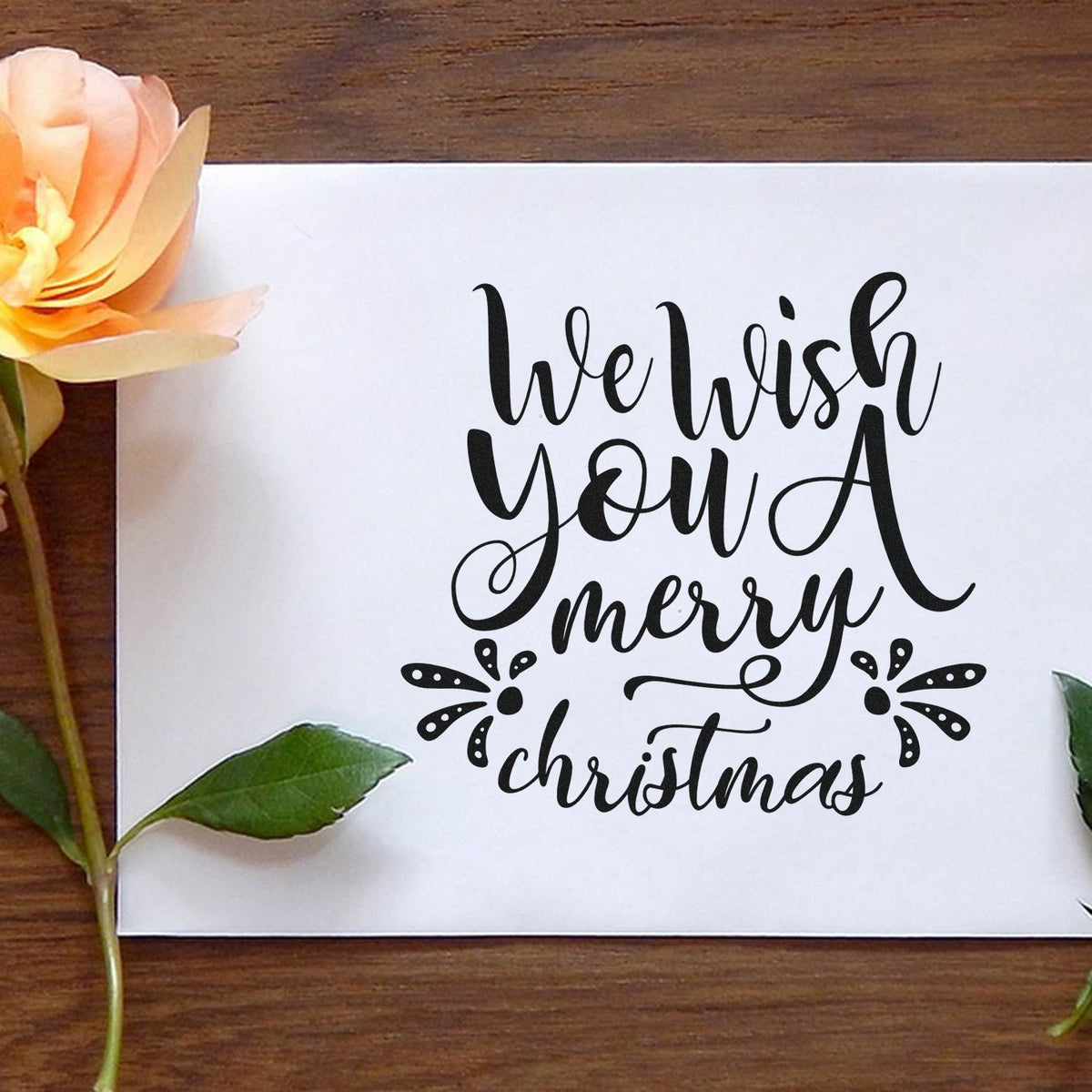 Black calligraphy stamp and seal reading We wish you a Merry Christmas on white paper with peach flower accents