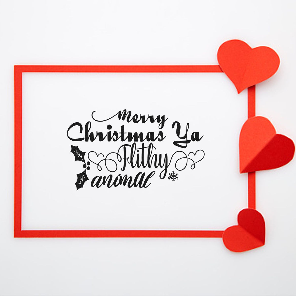 Black Merry Christmas Ya Filthy Animal stamp and seal design in red frame, with red paper hearts on white background