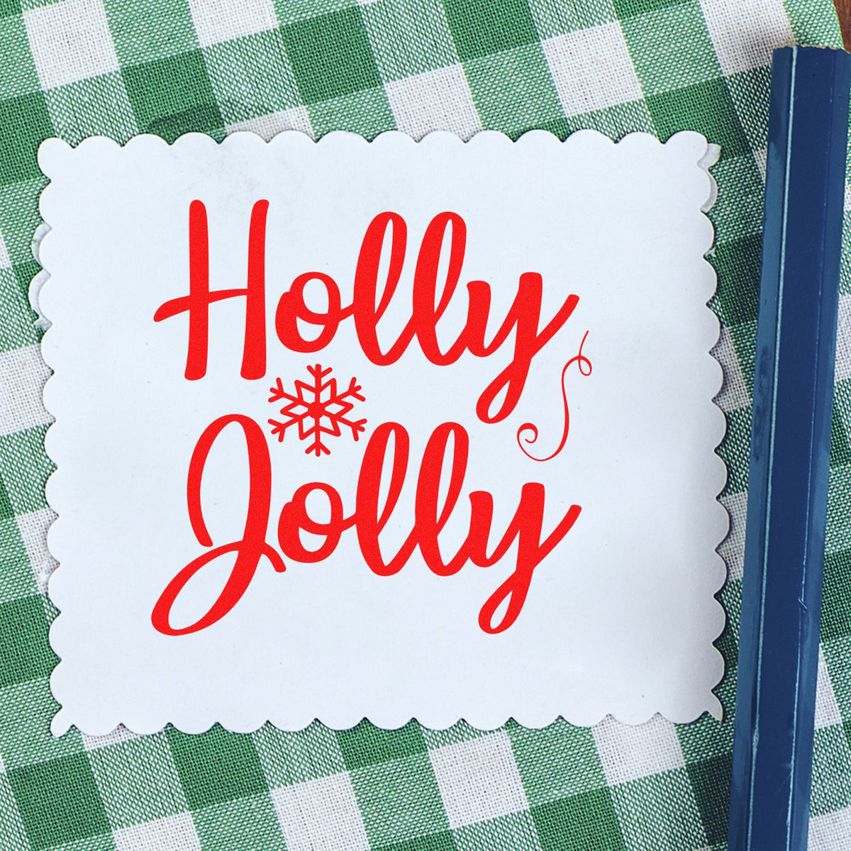 White scalloped holiday stamp seal with red Holly Jolly text and snowflake on green gingham background.