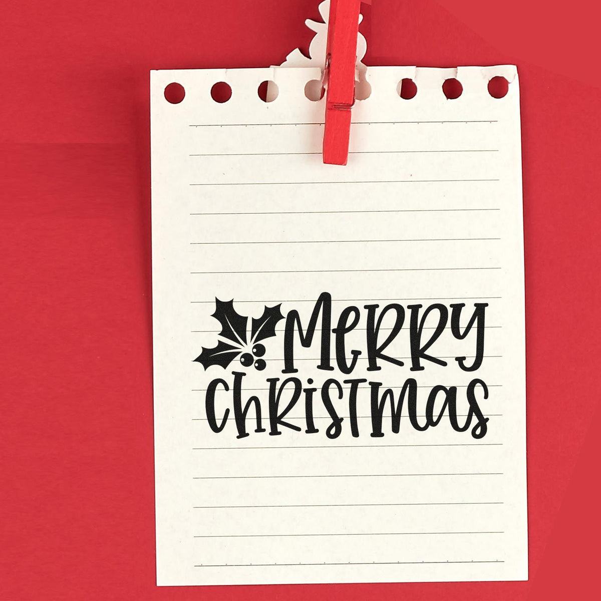 Merry Christmas stamp and seal design in black on lined white paper, clipped with a red clothespin on a red background.