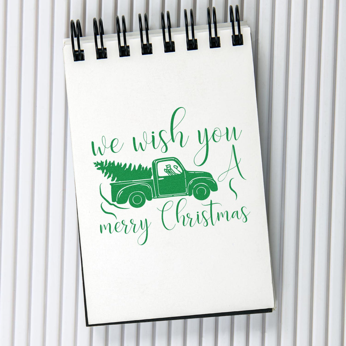 Green Christmas pickup truck stamp/seal design with We wish you a Merry Christmas on a white spiral notebook.
