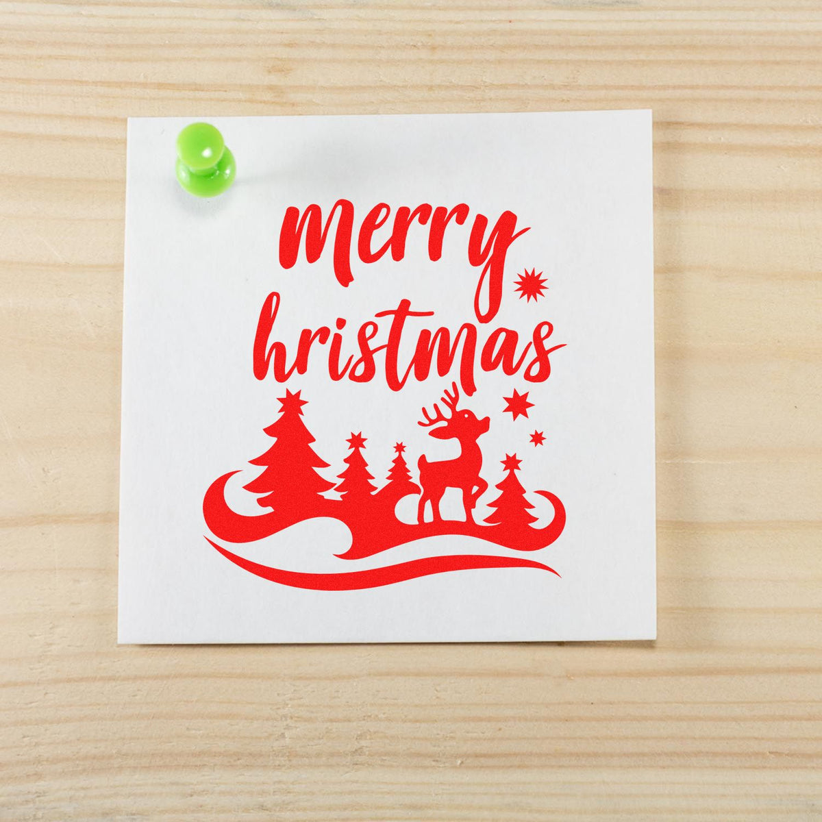 Red Merry Christmas stamp seal design with trees, reindeer and stars on white paper, pinned with a green pushpin