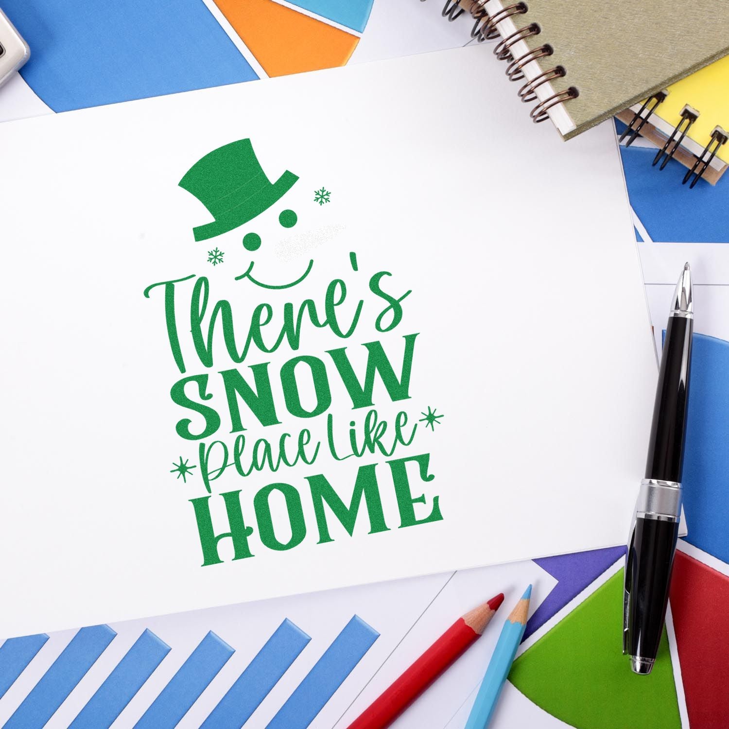 Green holiday stamp and seal design reading Theres Snow Place Like Home with snowman top hat on white paper.