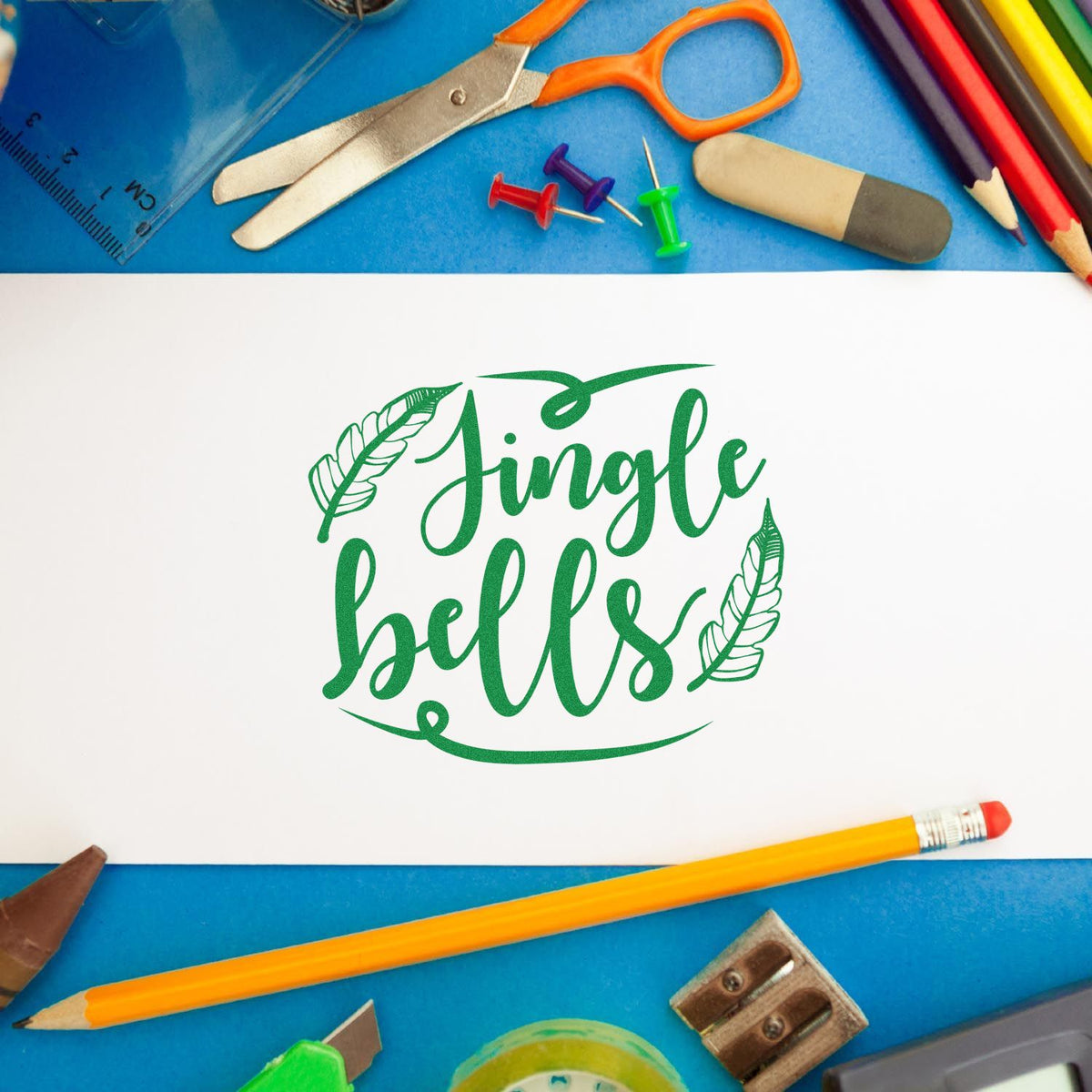 Green Jingle Bells stamp and seal design on white paper, with colorful school supplies on a blue background.